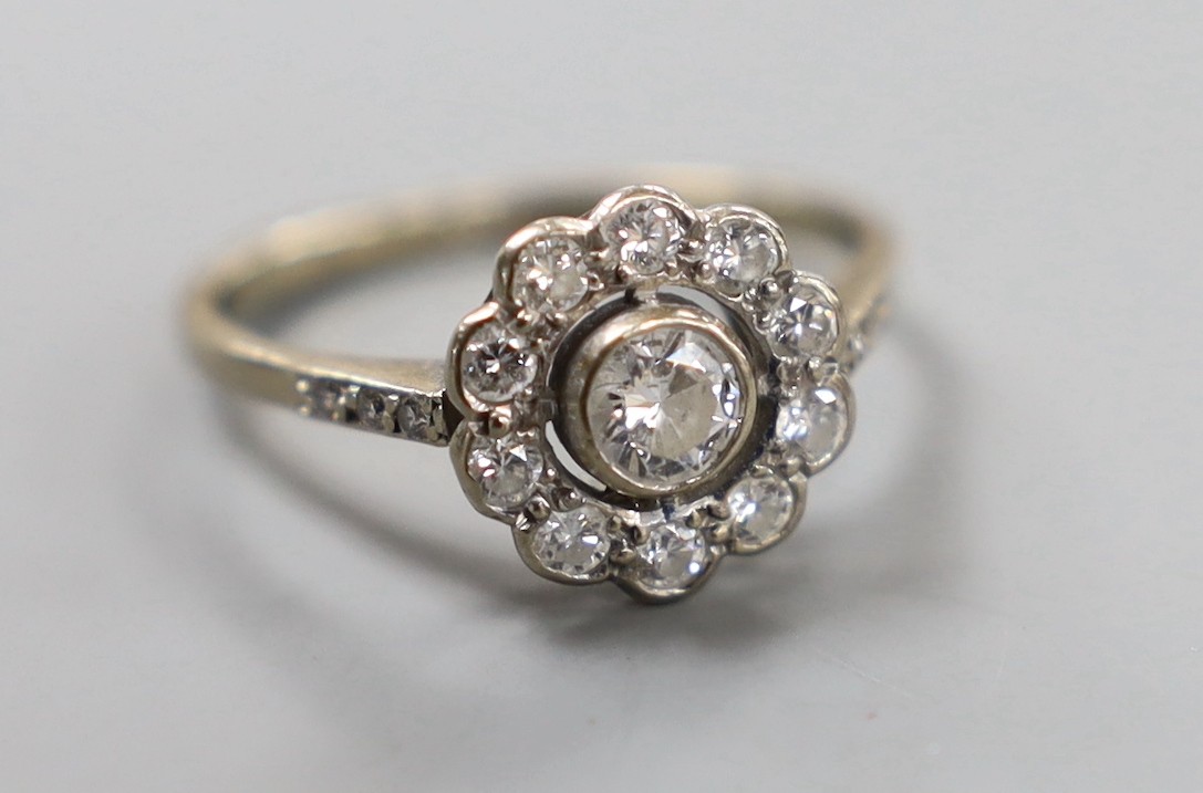 An 18ct white metal and eleven stone diamond set circular cluster ring, size N, gross weight 3.4 grams.
